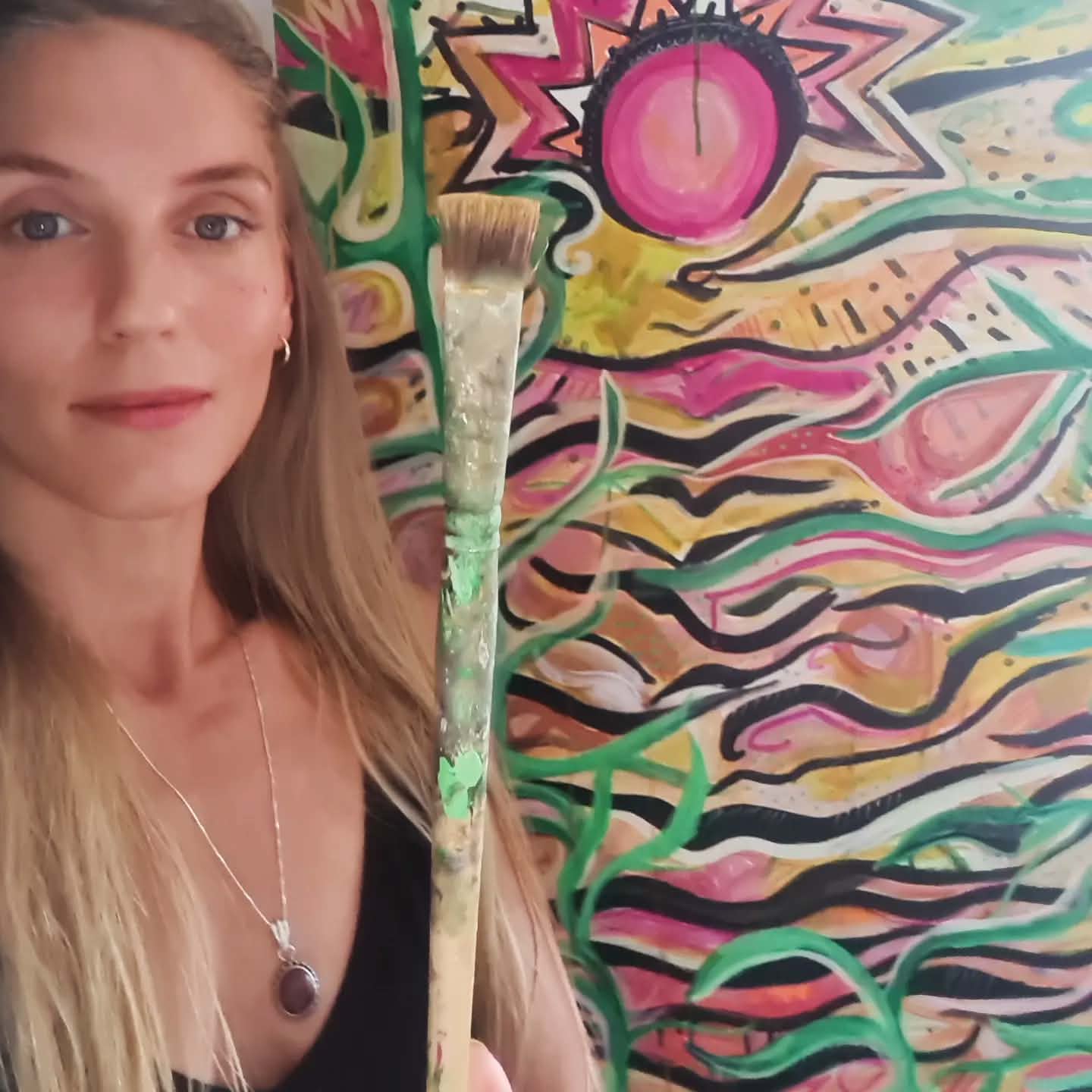Sas Dite holding a paintbrush beside her abstract artwork